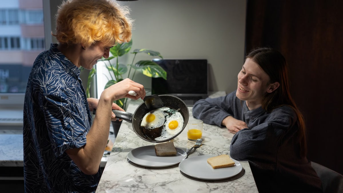 A happy couple preparing and enjoying a breakfast of eggs and toast in a cozy kitchen setting.
